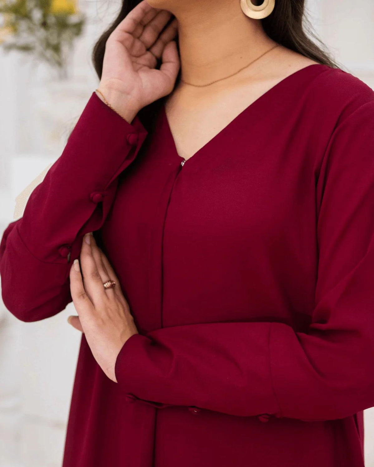 A close-up of a woman wearing a long-sleeve magenta dress with a V-neckline and decorative buttons along the front and cuffs.