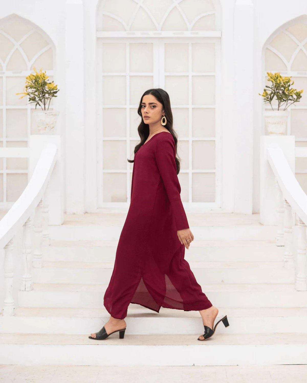 A woman wearing a long-sleeved magenta co ord set walks down white stone steps in front of a white building with arched windows.