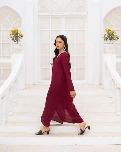 A woman wearing a long-sleeved magenta co ord set walks down white stone steps in front of a white building with arched windows.