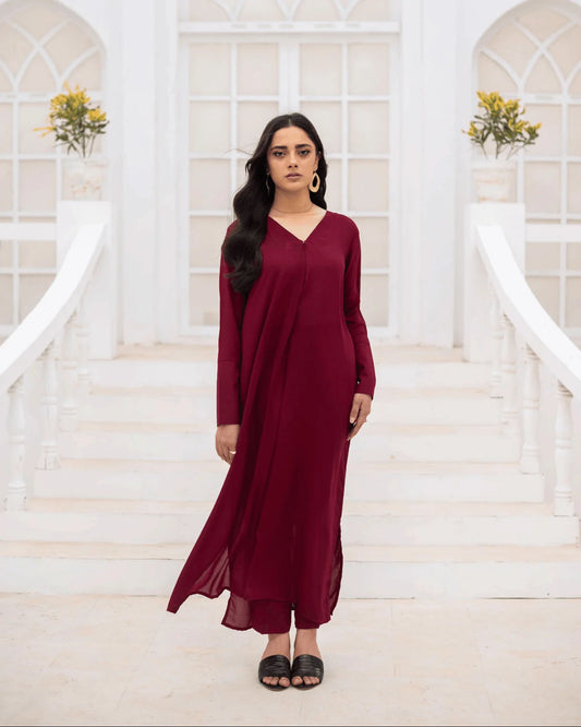 A woman wearing a long-sleeved, floor-length co ord set stands on white stone steps in front of a white arched building.