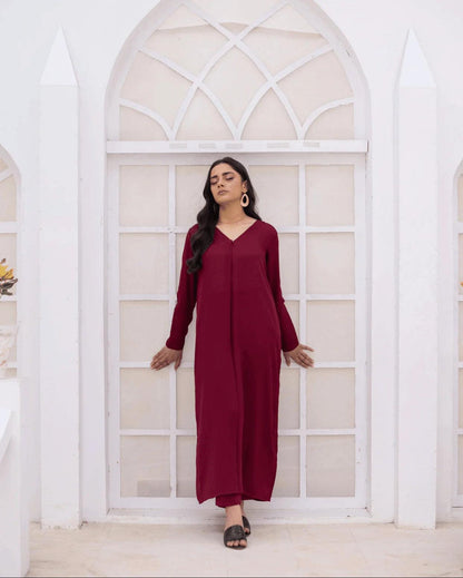 A woman wearing a long-sleeved magenta co ord set stands in front of a white arched window frame.