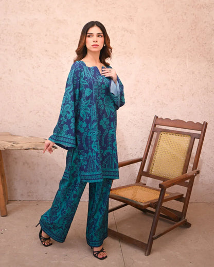 Women standing beside a chair wearing a floral printed two piece dress which includes a shirt and culotte.