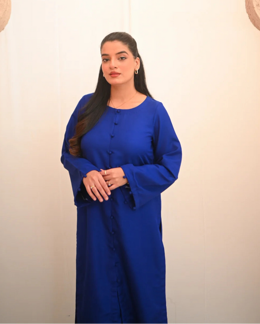 A woman standing and posing in a blue two-piece rawsilk dress with a shirt and straight trousers.