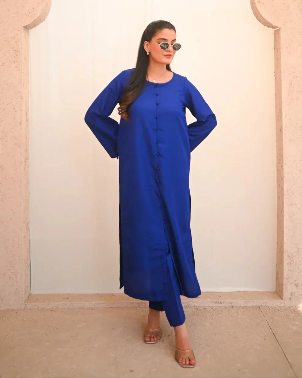 A woman standing and posing in a blue two-piece rawsilk dress with a shirt and straight trousers.