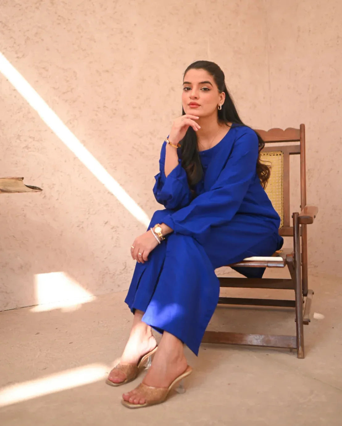 A woman Sitting and posing in a blue two-piece rawsilk dress with a shirt and straight trousers.