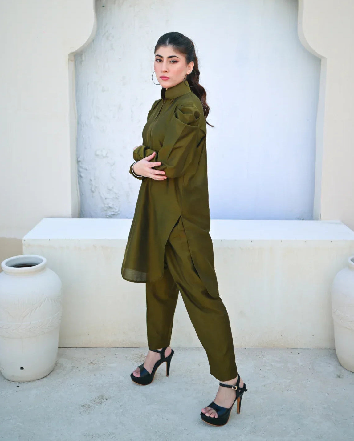 Woman in a green outfit standing in front of a decorative wall with white pots.