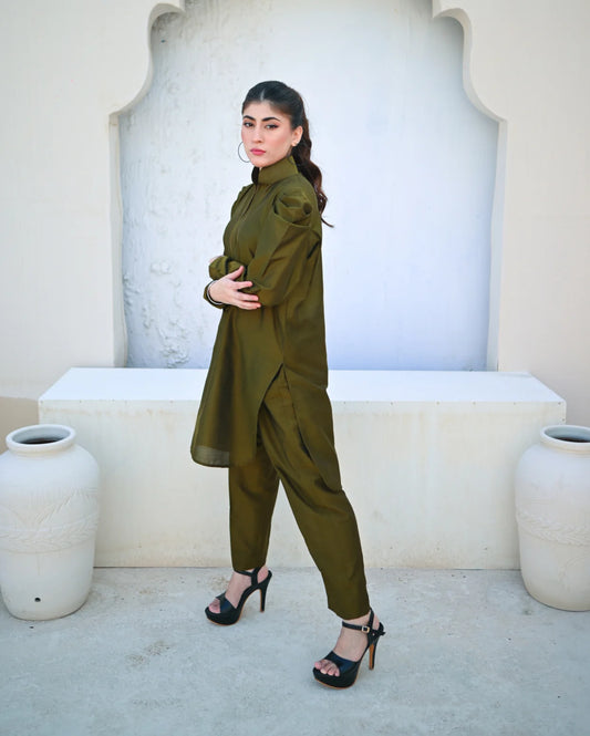 Woman in a green outfit standing in front of a decorative wall with white pots.