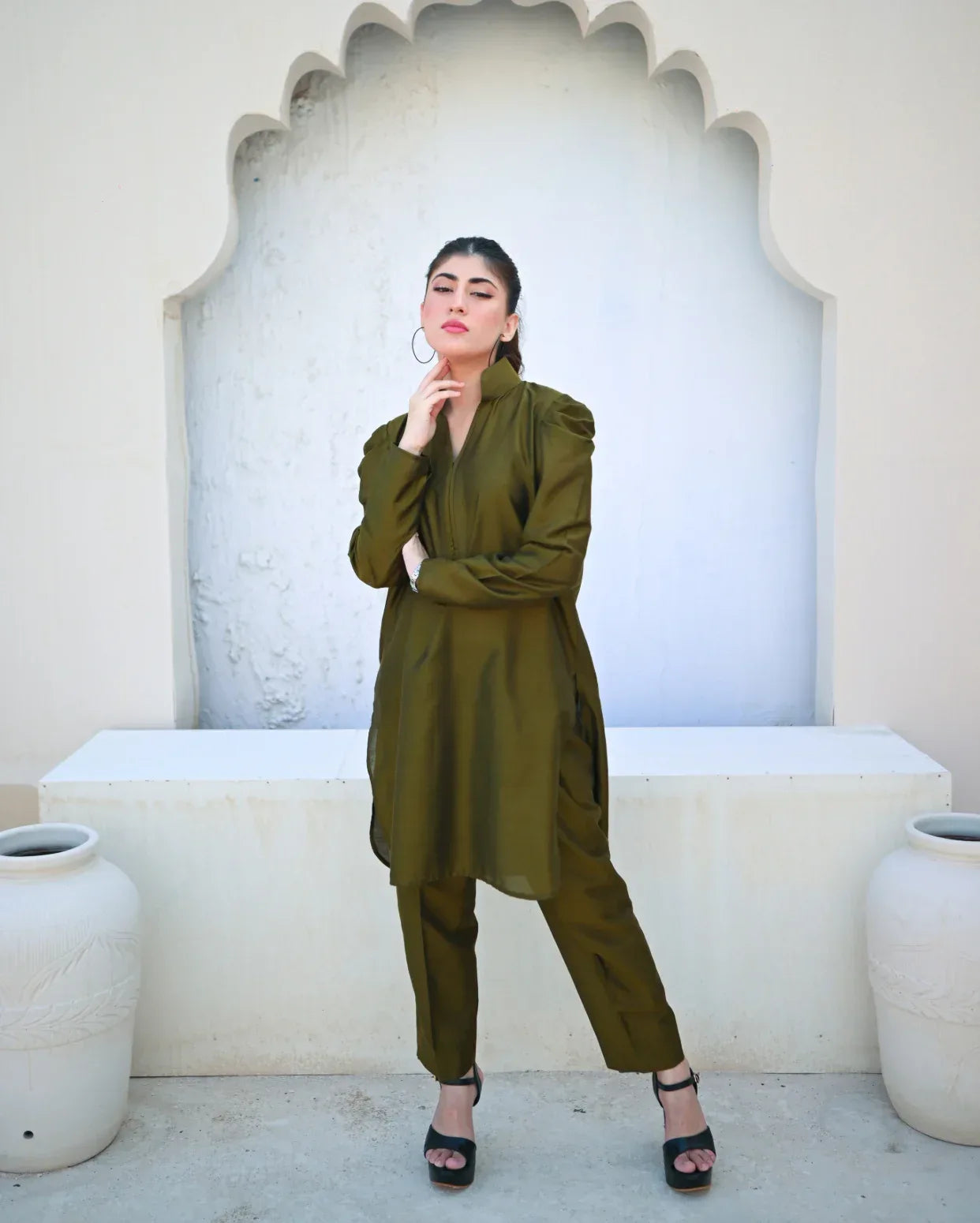 Woman in a green outfit standing in front of an arched white wall.
