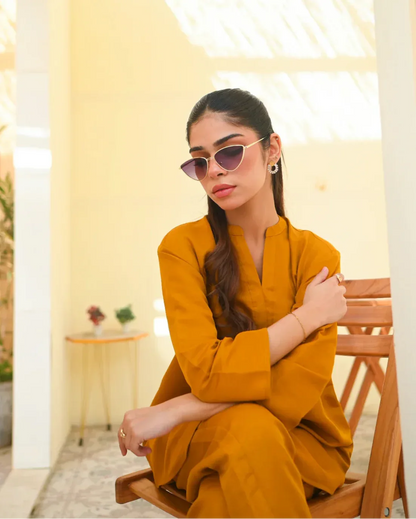 A woman wearing a mustard yellow two-piece dress with long sleeves, consisting of a shirt and trousers.