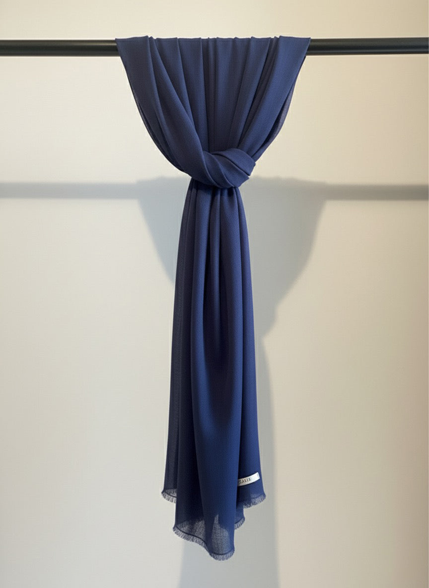 Navy blue scarf draped over a black rod against a beige wall.