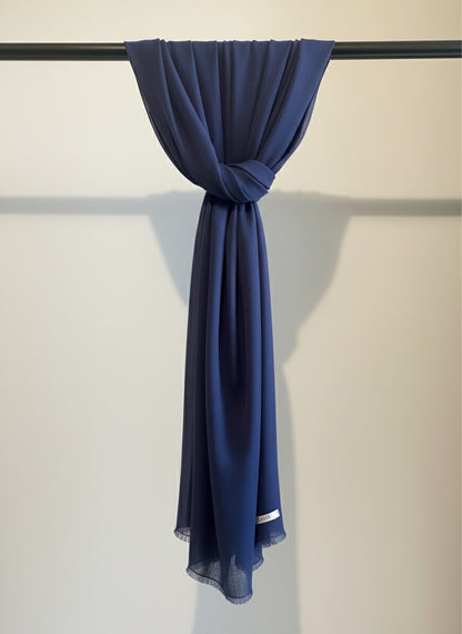 Navy blue scarf draped over a black rod against a beige wall.