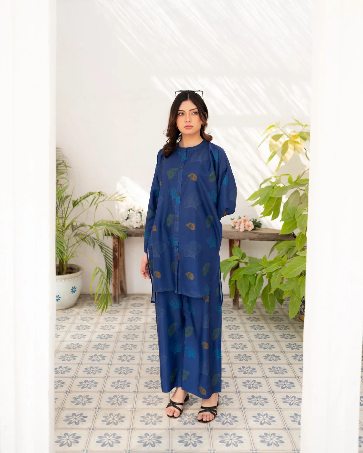 Woman wearing a navy blue outfit with leaf patterns in a room with plants and a tiled floor.