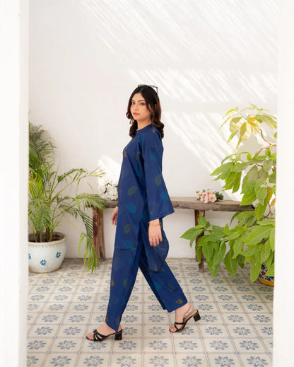 Woman in a navy blue outfit standing in a room with plants and a tiled floor.