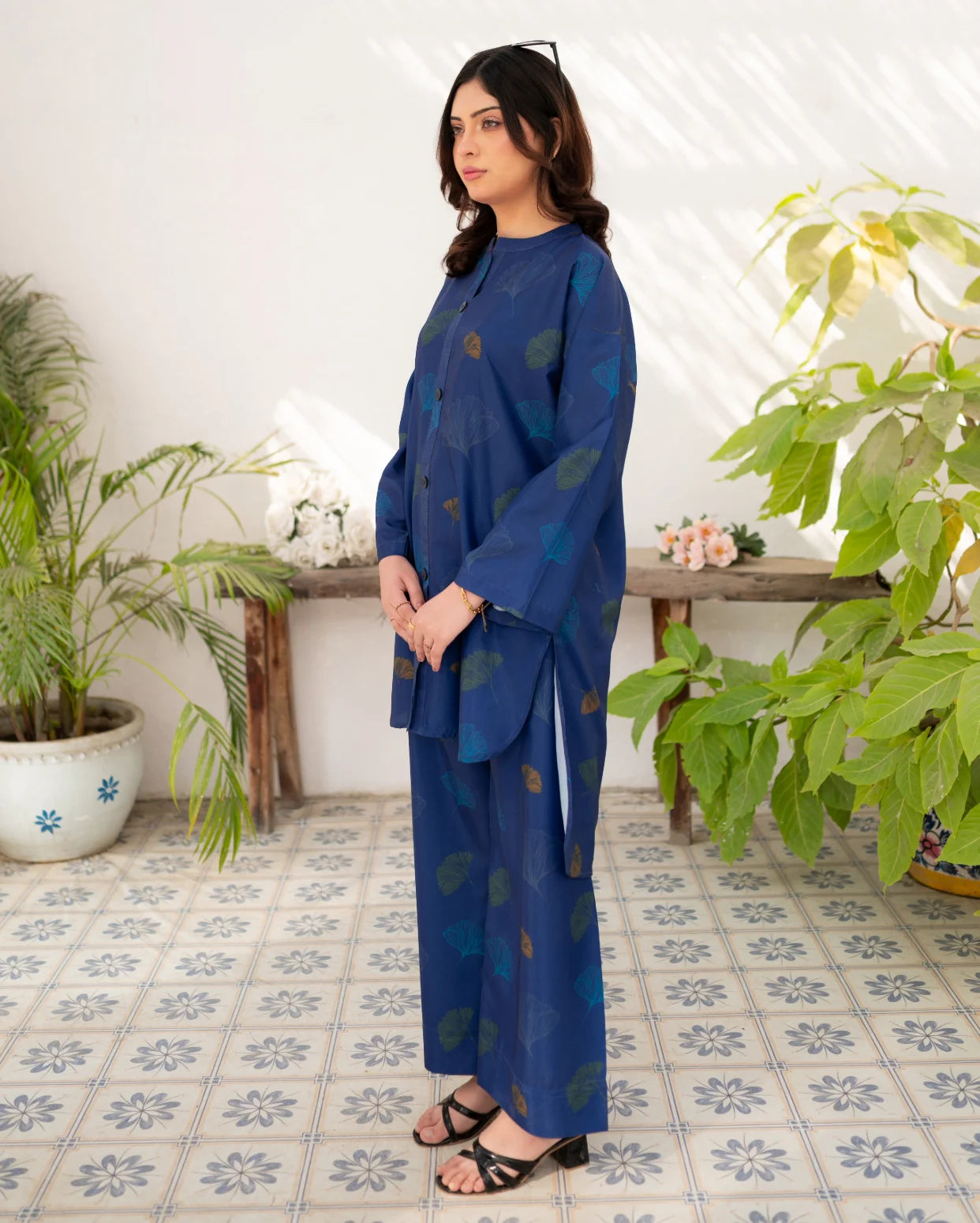 Woman in a navy blue outfit standing in a room with plants and a tiled floor.