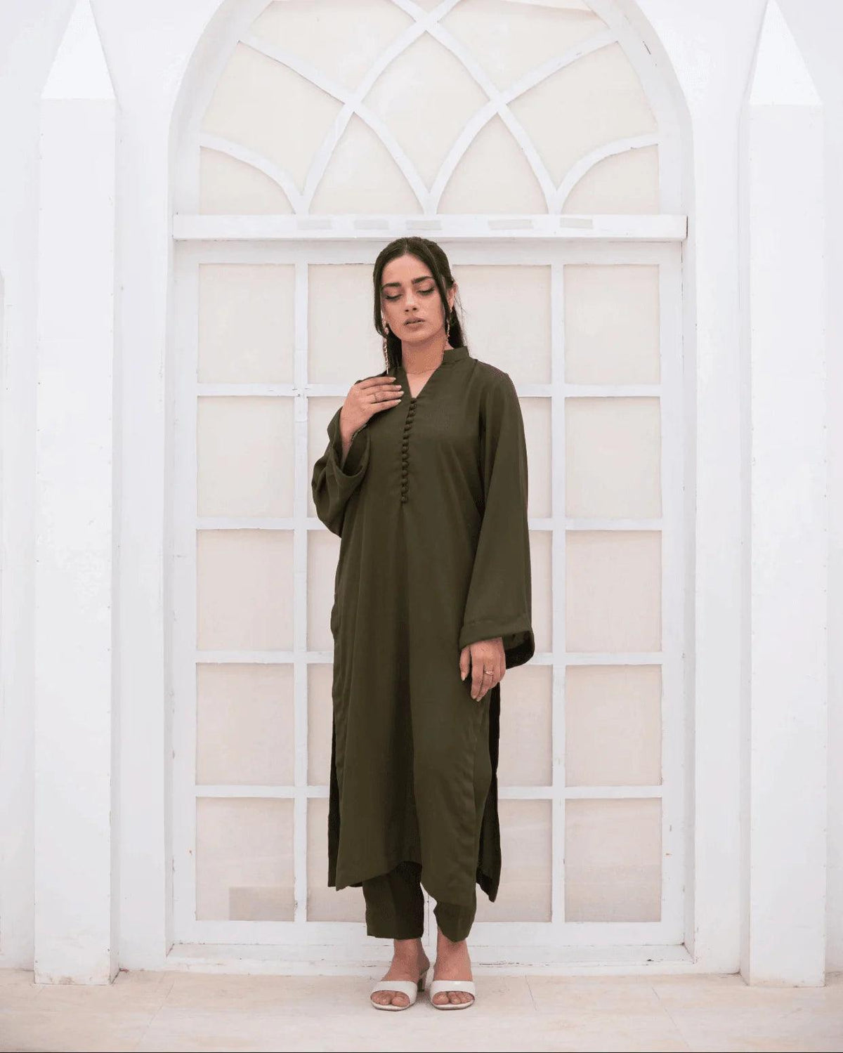 A woman wearing an olive green long-sleeve co ord set stands in front of a white arched window.