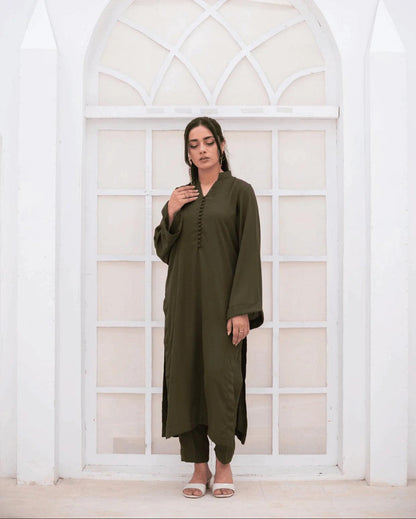 A woman wearing an olive green long-sleeve co ord set stands in front of a white arched window.