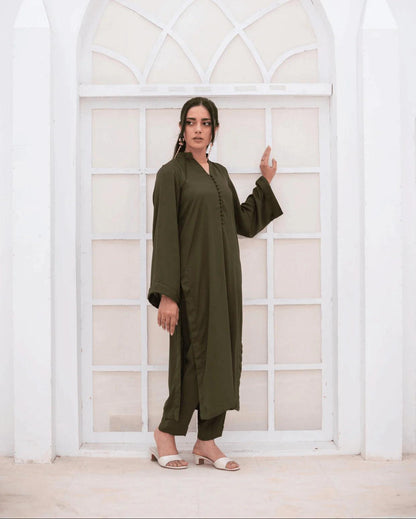 A woman wearing an olive green long-sleeve co ord set stands in front of a white arched window.