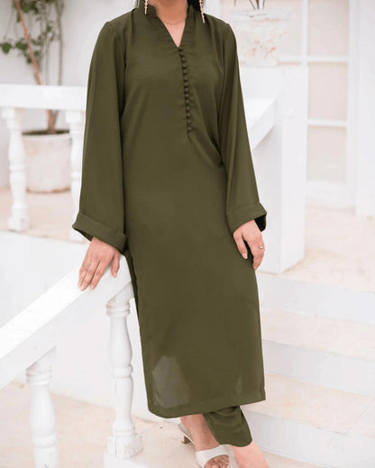 A woman wearing a long olive green co ord set, standing on white stairs in a bright indoor setting.
