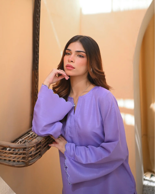 A woman wearing a purple two-piece rawsilk dress with embroidered details. The dress includes a shirt with long sleeves and matching culotte.