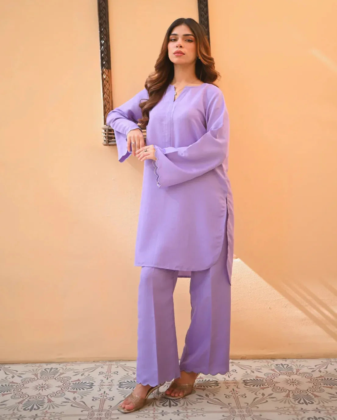 A woman wearing a purple two-piece rawsilk dress with embroidered details. The dress includes a shirt with long sleeves and matching culotte.
