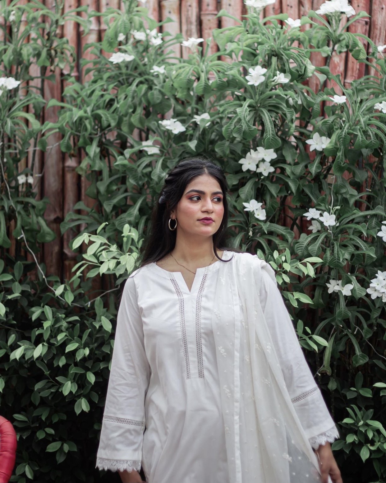 A woman in white three piece dress outdoor on a sunny day, surrounded by greenery.