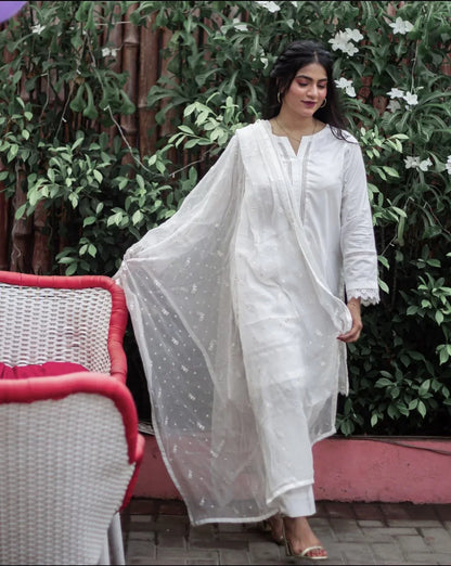 A woman in white three piece dress walking outdoor on a sunny day, surrounded by greenery.