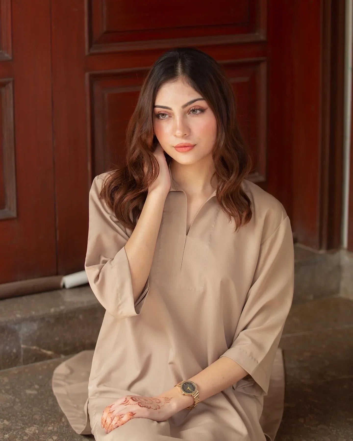 A woman in a Phone Dress sitting in front of large wooden doors with a thoughtful expression. 