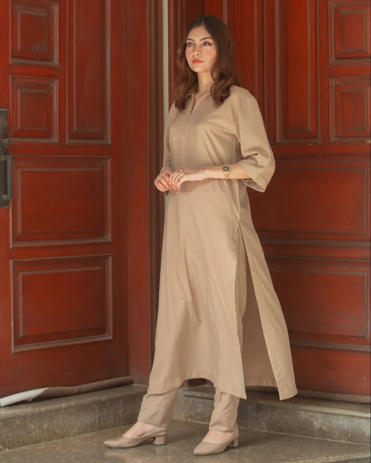 A woman in a Phone Dress stands in front of large wooden doors with a thoughtful expression. 