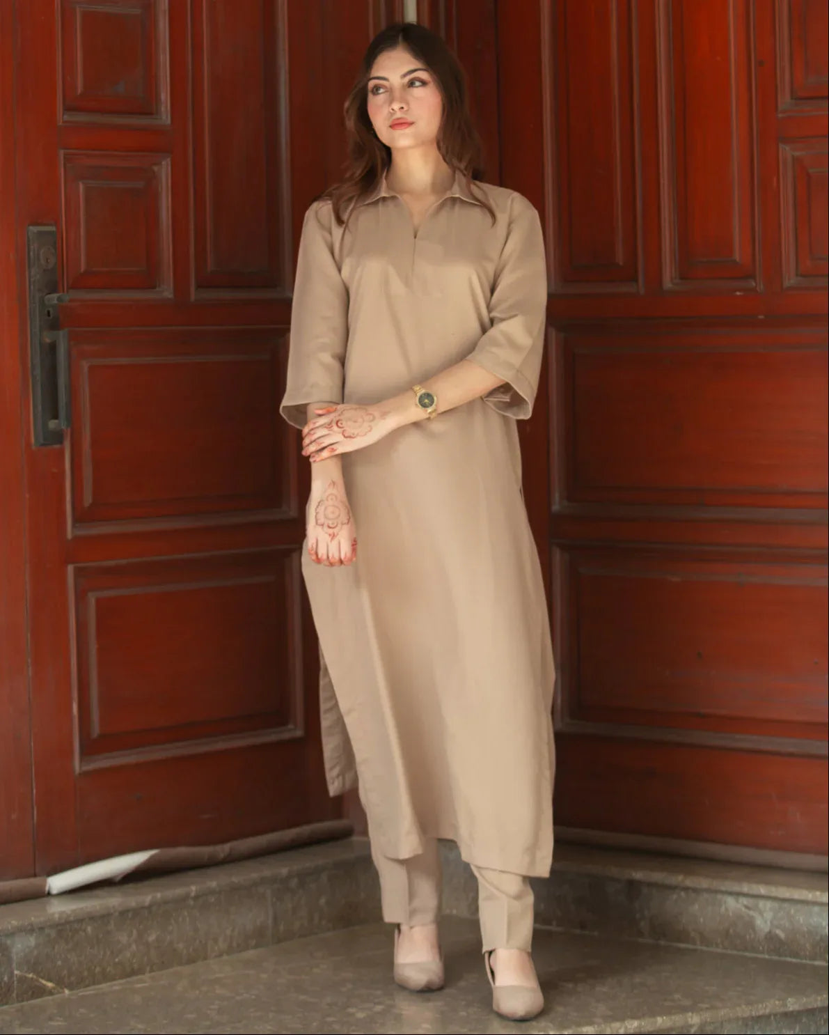 A woman in a Phone Dress stands in front of large wooden doors with a thoughtful expression. 