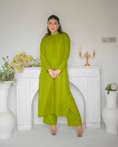 Woman in a green dress standing in a room with white walls and decorative elements. it is a simple dress for mehndi.