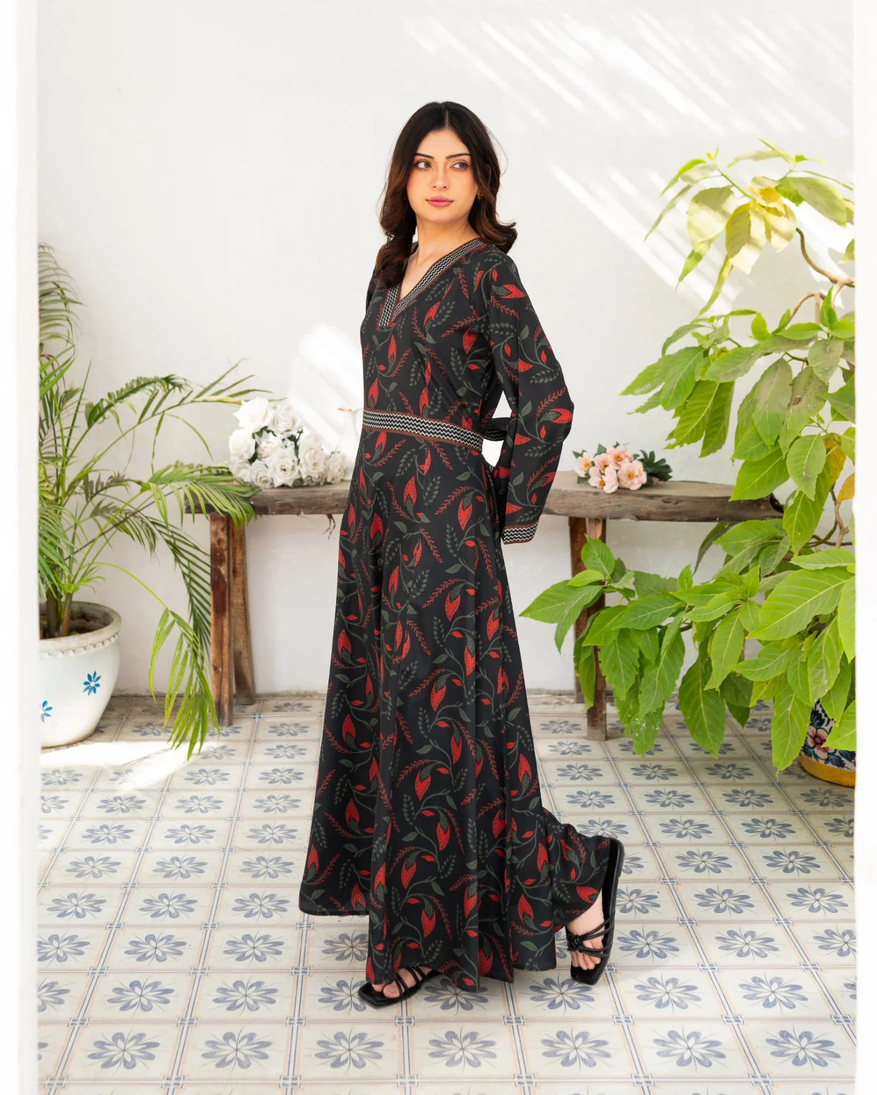 Woman wearing a black dress with floral print in a room with plants and a wooden table.
