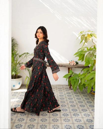 Woman in a black dress floral print standing in a room with plants and a bench.