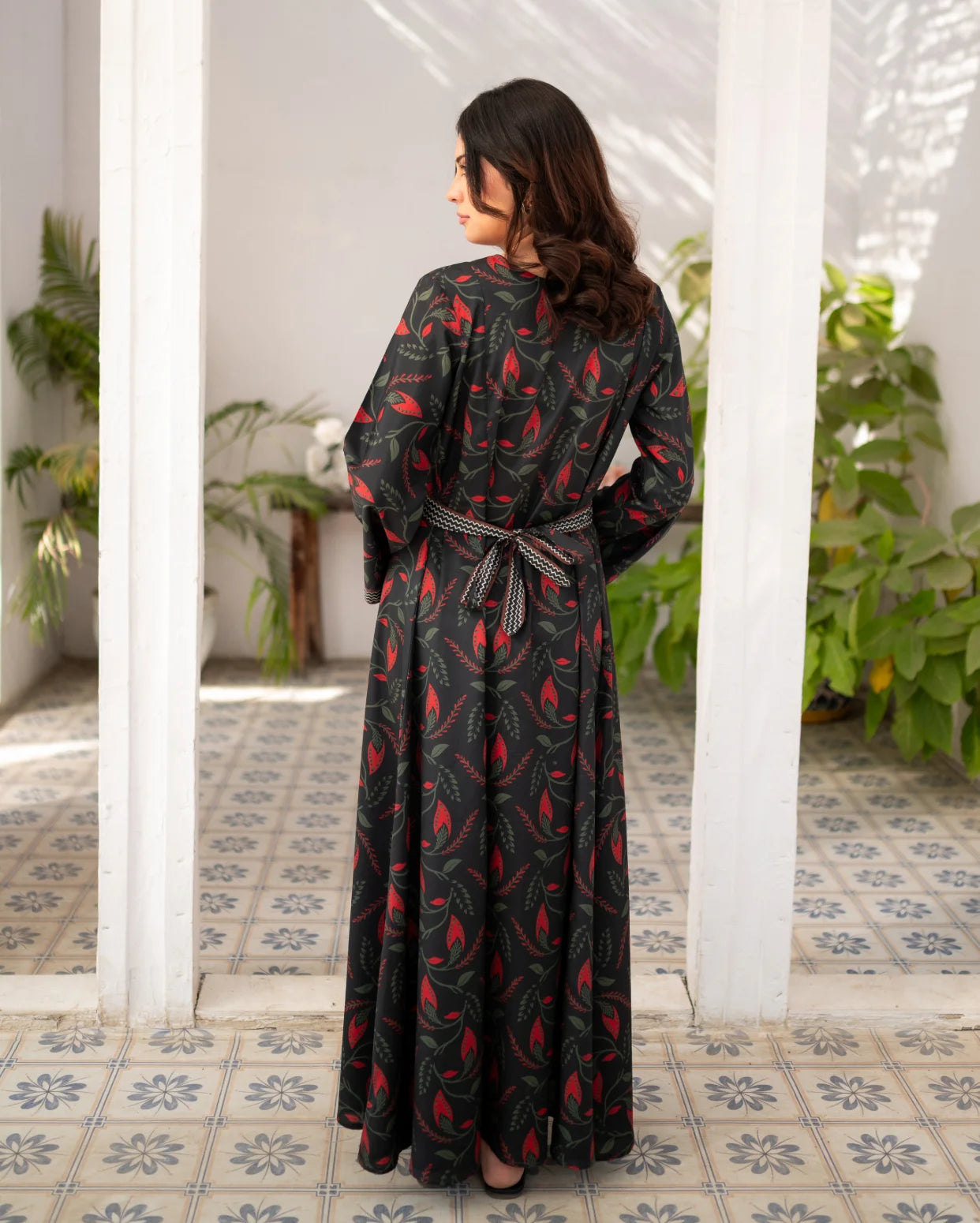 Woman wearing a black printed dress with a belt in a room with white walls and tiled floor.