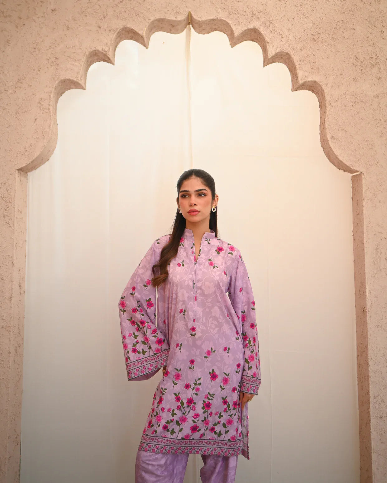 Woman wearing a pink floral outfit standing in front of an archway.