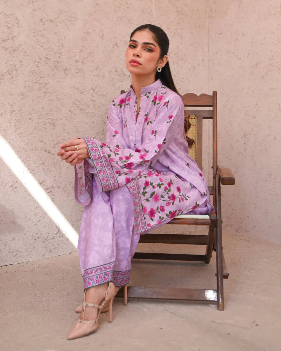 Woman sitting on a chair wearing a pink floral printed dress which includes a shirt and shalwar.