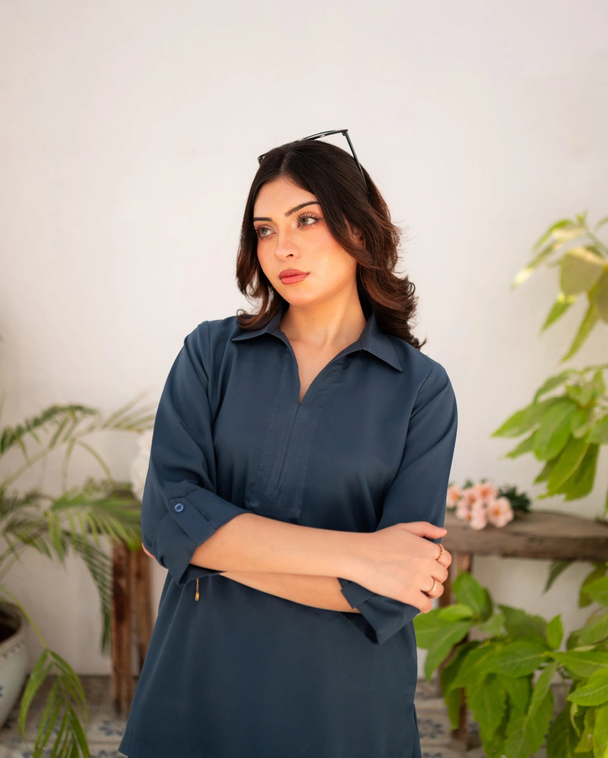 Woman wearing a steel blue shirt standing in a room with plants