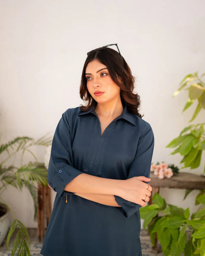 Woman wearing a steel blue shirt standing in a room with plants