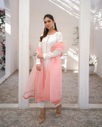 A woman wearing a three piece rawsilk dress with an ombre shirt, trousers, and an organza dupatta in pink and white colors.