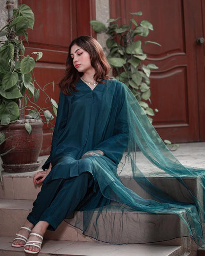 Woman in a teal blue dress sitting in front of a wooden door with plants around.