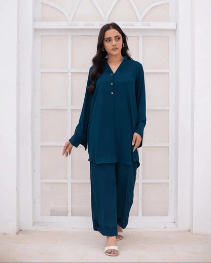 A woman modeling a teal blue co ord set with a V-neck long-sleeve, standing in front of a white arched window frame.
