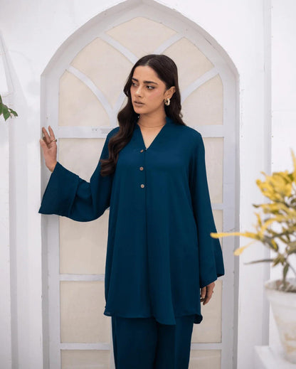 A woman modeling a teal blue co ord set, standing in front of a white arched door frame.