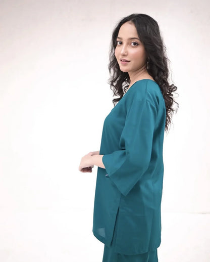 Woman wearing a teal green outfit standing against a white background