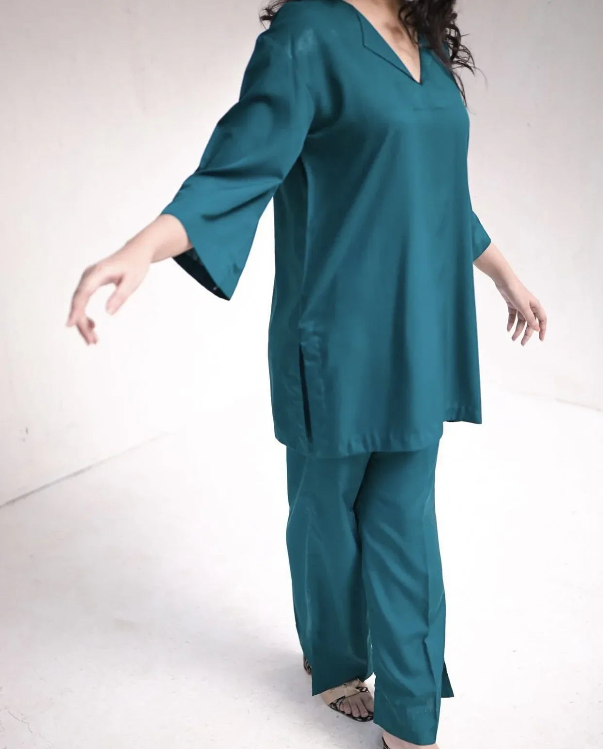 Woman wearing a teal green outfit standing against a white background