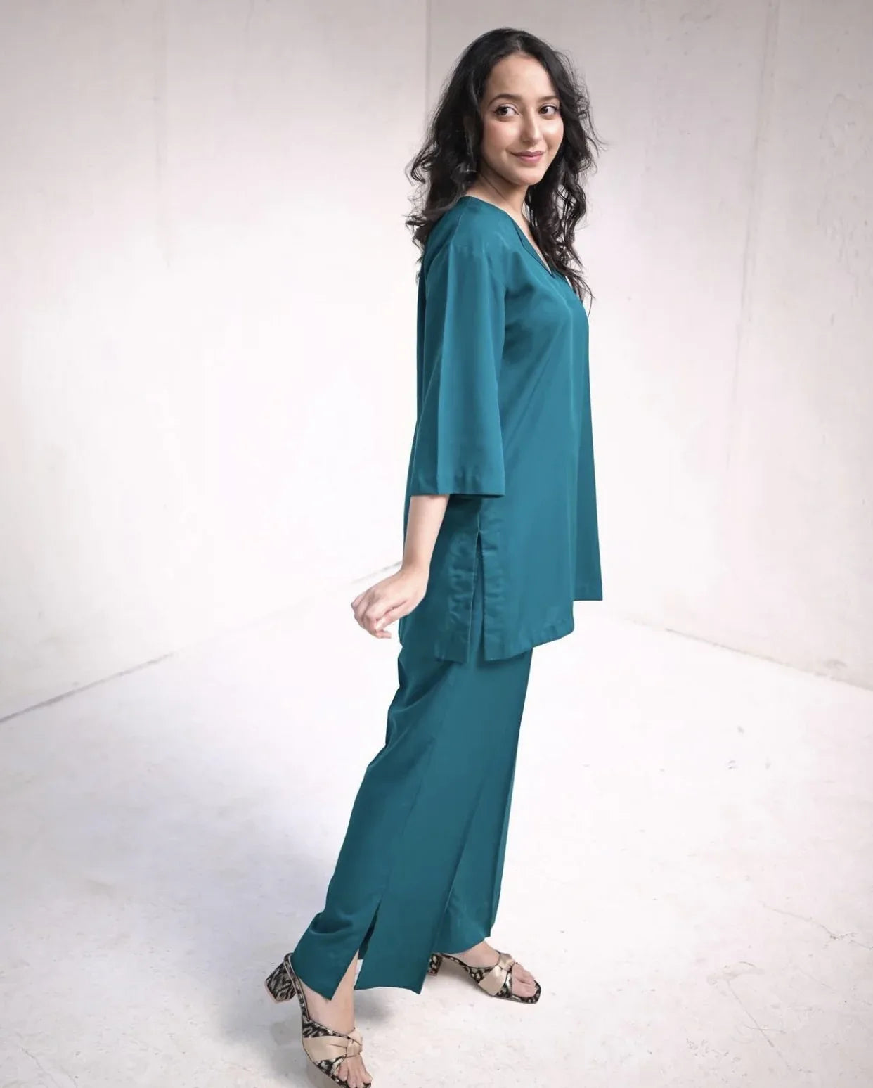 Woman wearing a teal green outfit standing against a white background