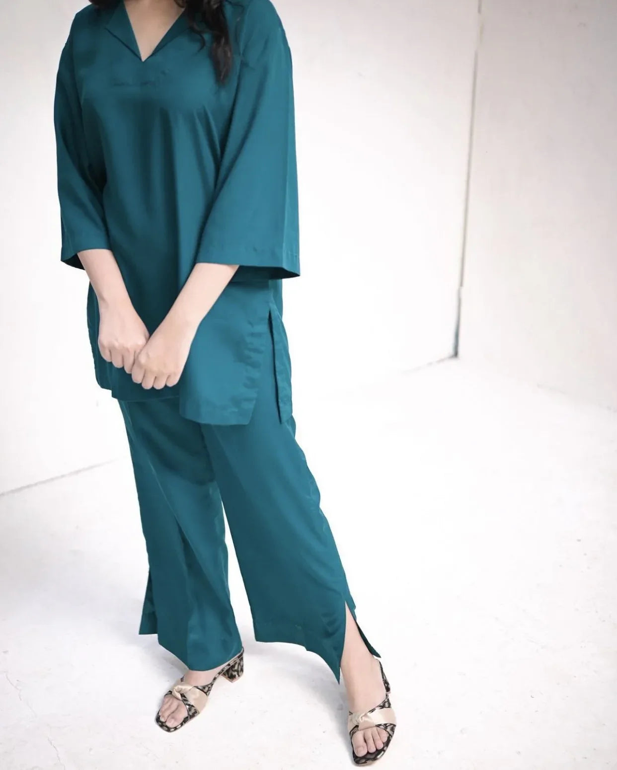 Woman wearing a teal green outfit standing against a white background