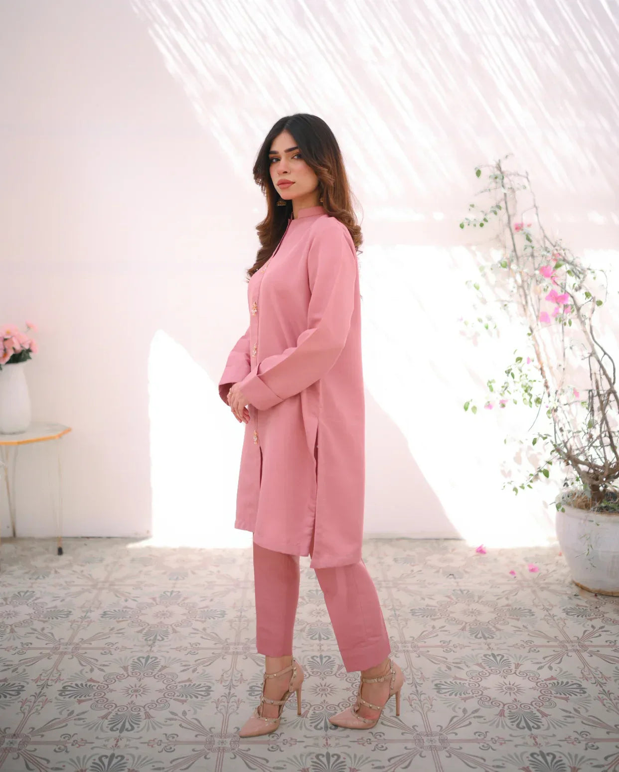 A woman wearing a pink two-piece indian rawsilk dress consisting of a shirt and trousers.
