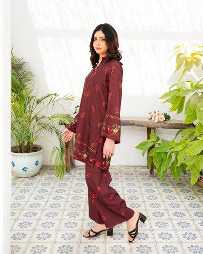 Woman wearing a maroon floral outfit standing in a room with plants and a bench.