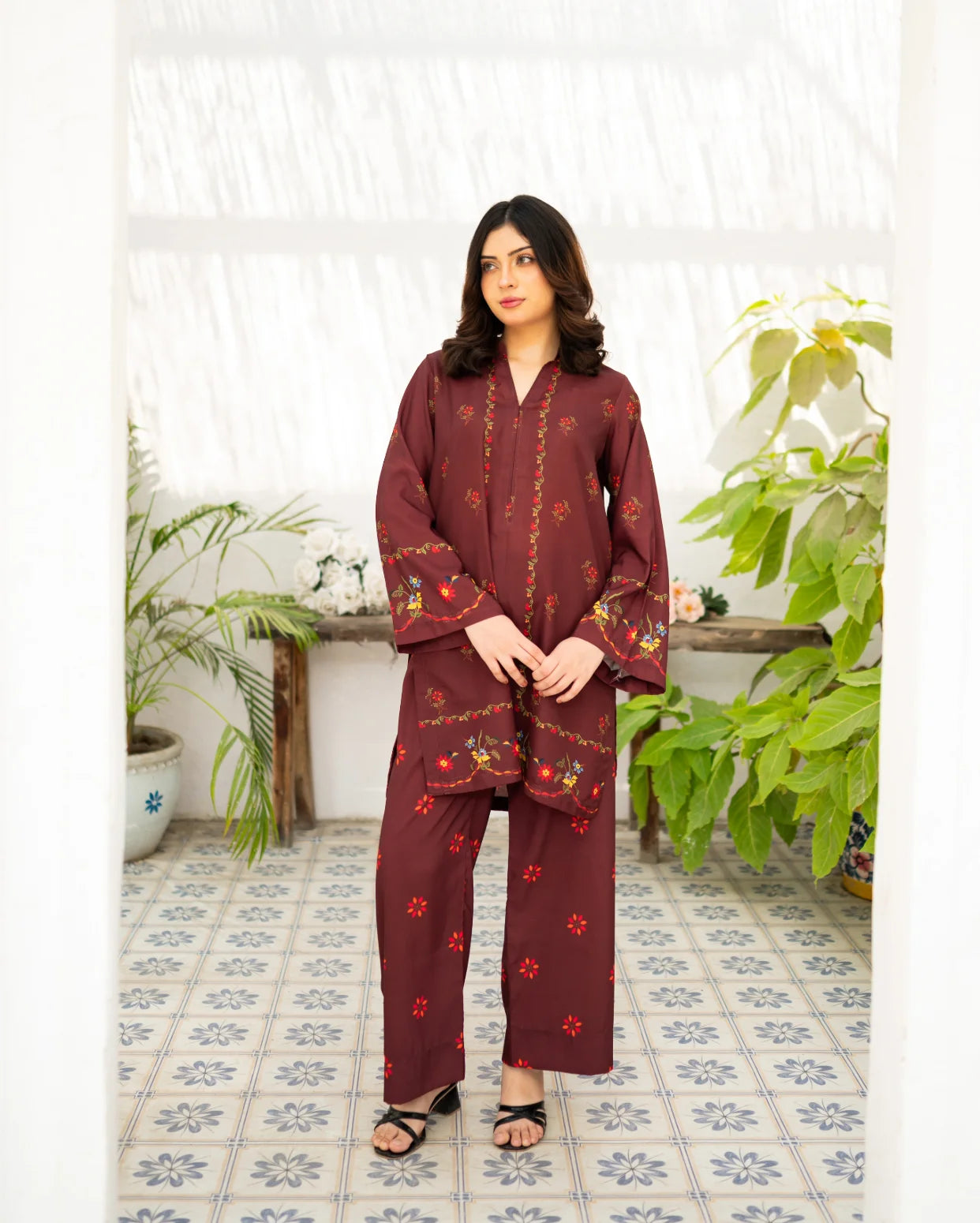 Woman wearing a maroon outfit in a room with plants and a tiled floor.