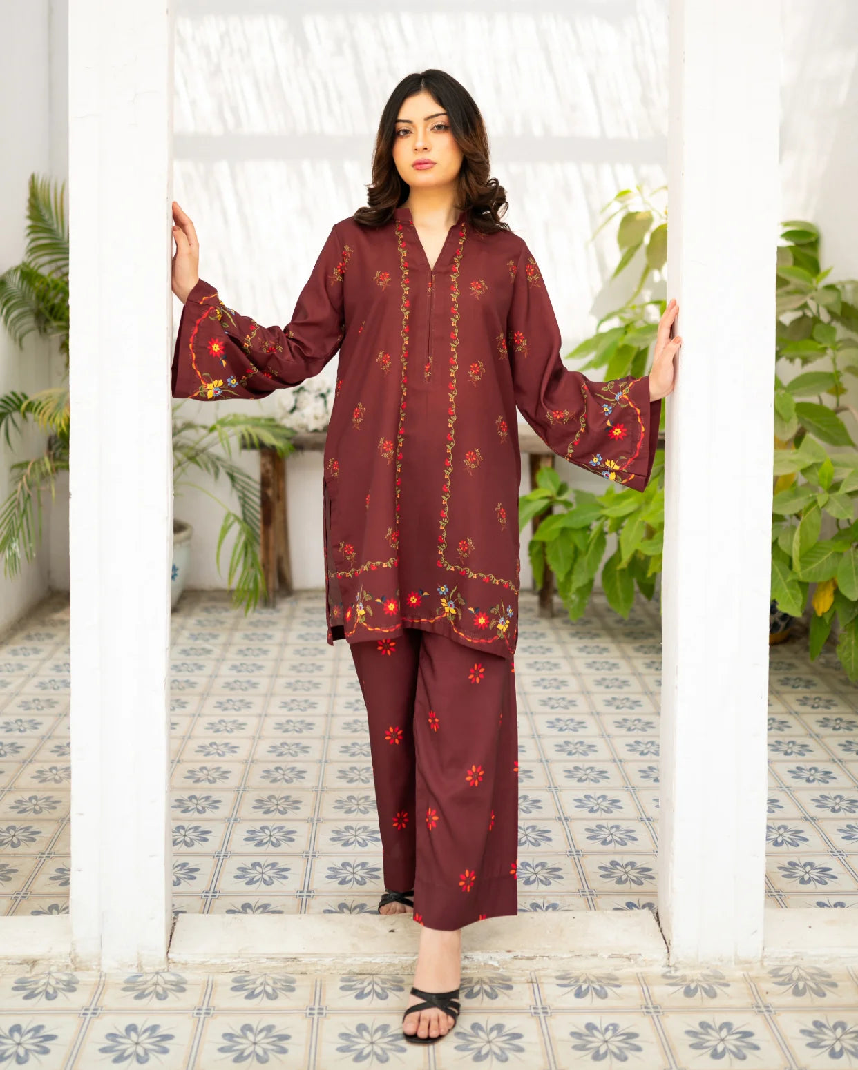 Woman wearing a maroon traditional outfit with floral patterns in a decorated room.