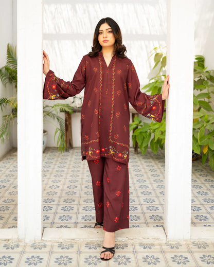 Woman wearing a maroon traditional outfit with floral patterns in a decorated room.